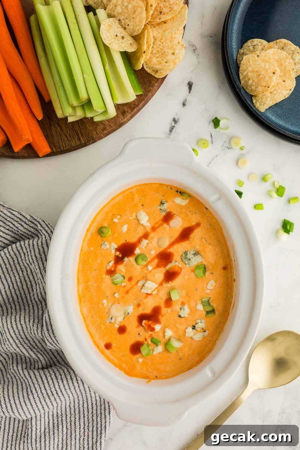Slow Cooker Buffalo Chicken Dip: Creamy Cheesy Party Recipe 2 Cheesy Slow Cooker Buffalo Chicken Dip garnished and in bowl next to dish of celery, carrots, and tortilla chops