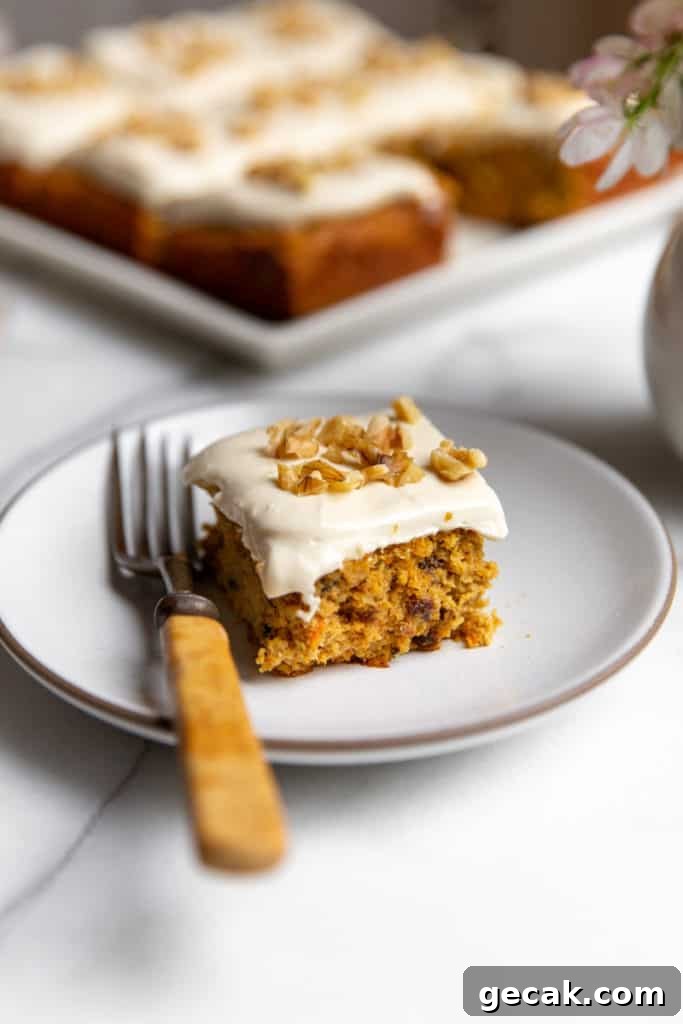 A piece of carrot cake on a plate with a fork, topped with maple cream cheese frosting. 