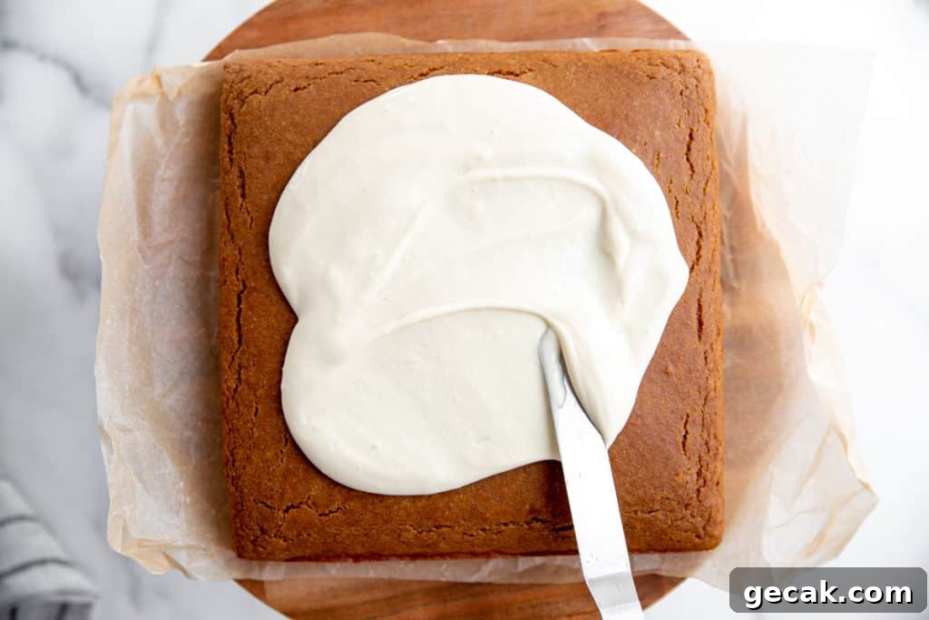 A spatula spreading maple cream cheese frosting over a cake. 