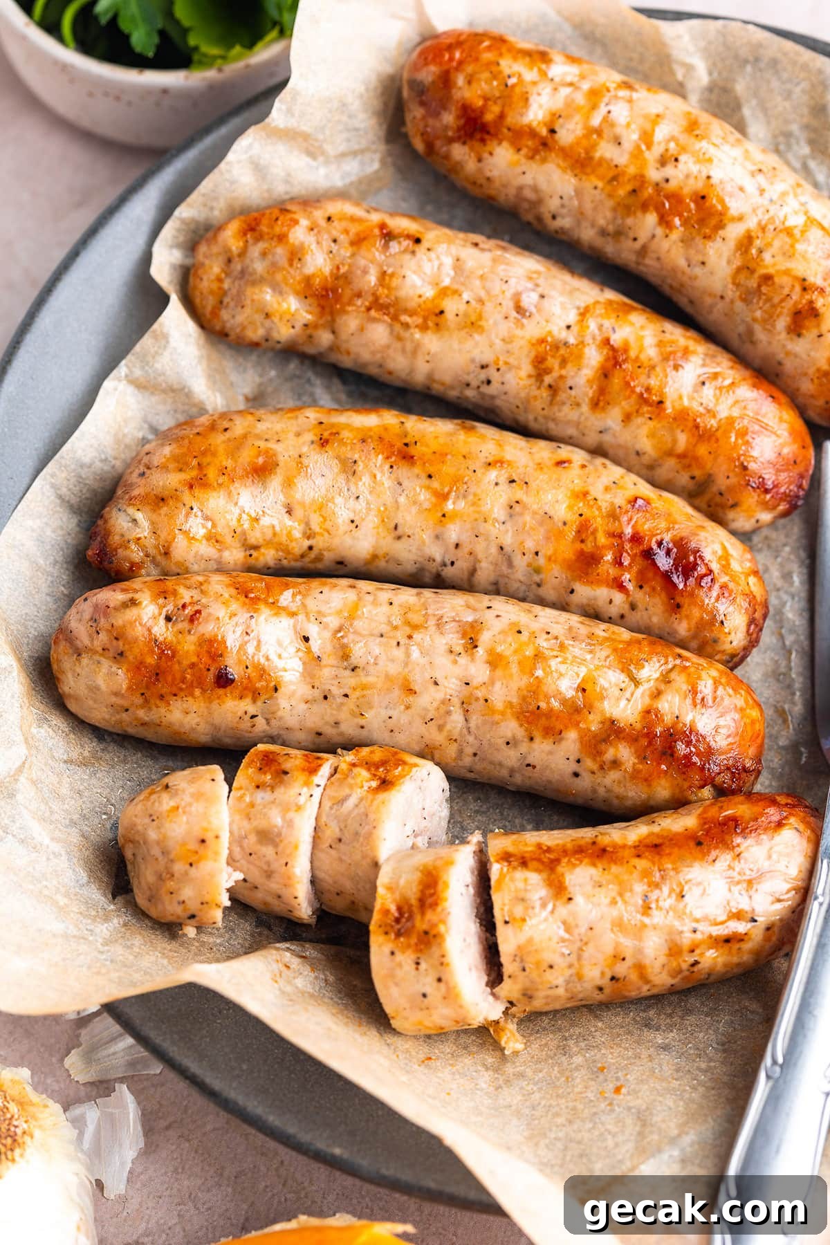 Crispy Air Fryer Italian Sausage Recipe for Quick Dinner 3 5 Italian sausages on a plate lined with parchment paper. One of the sausages is sliced into thick discs.