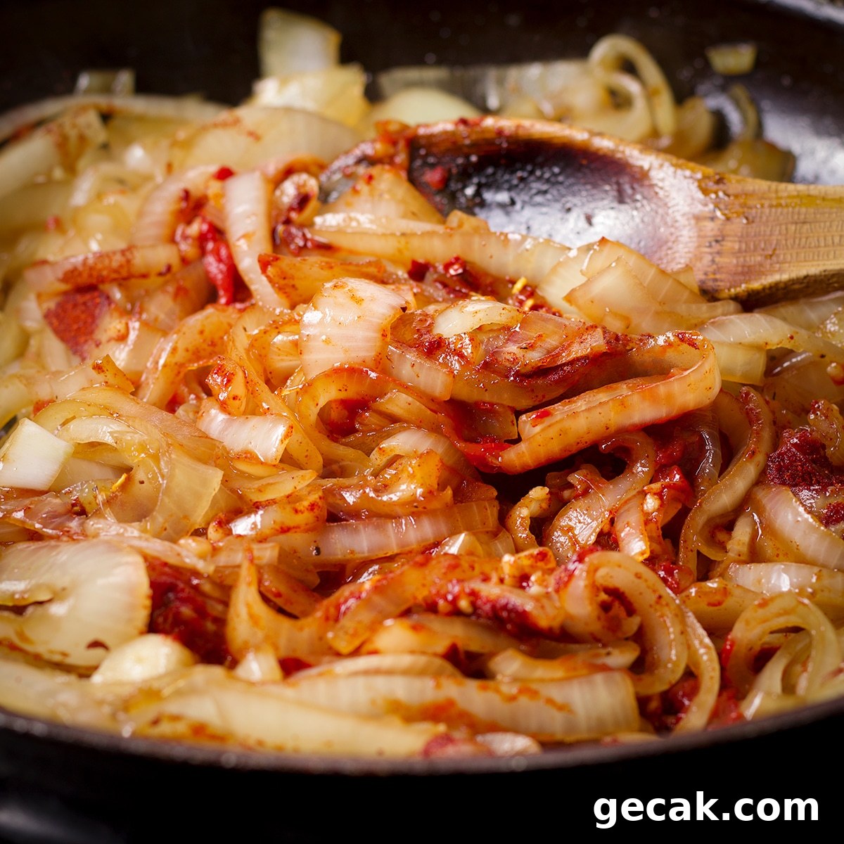 Using a wooden spoon to stir tomato paste and spices into onions as they cook in a skillet.