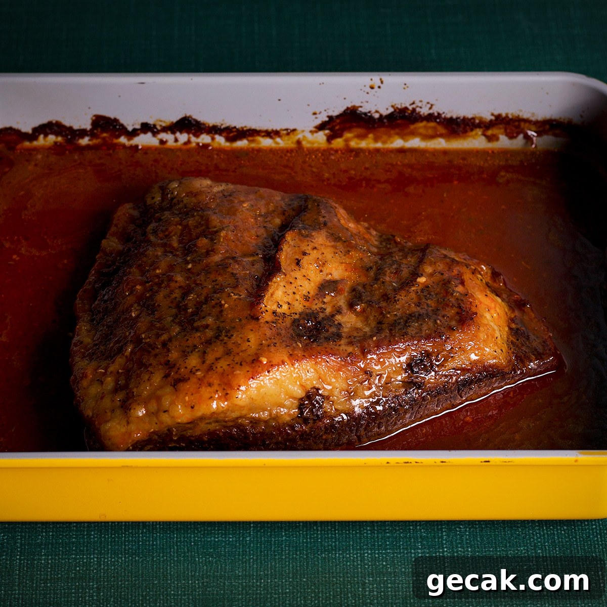 A cooked brisket in a pan with sauce.