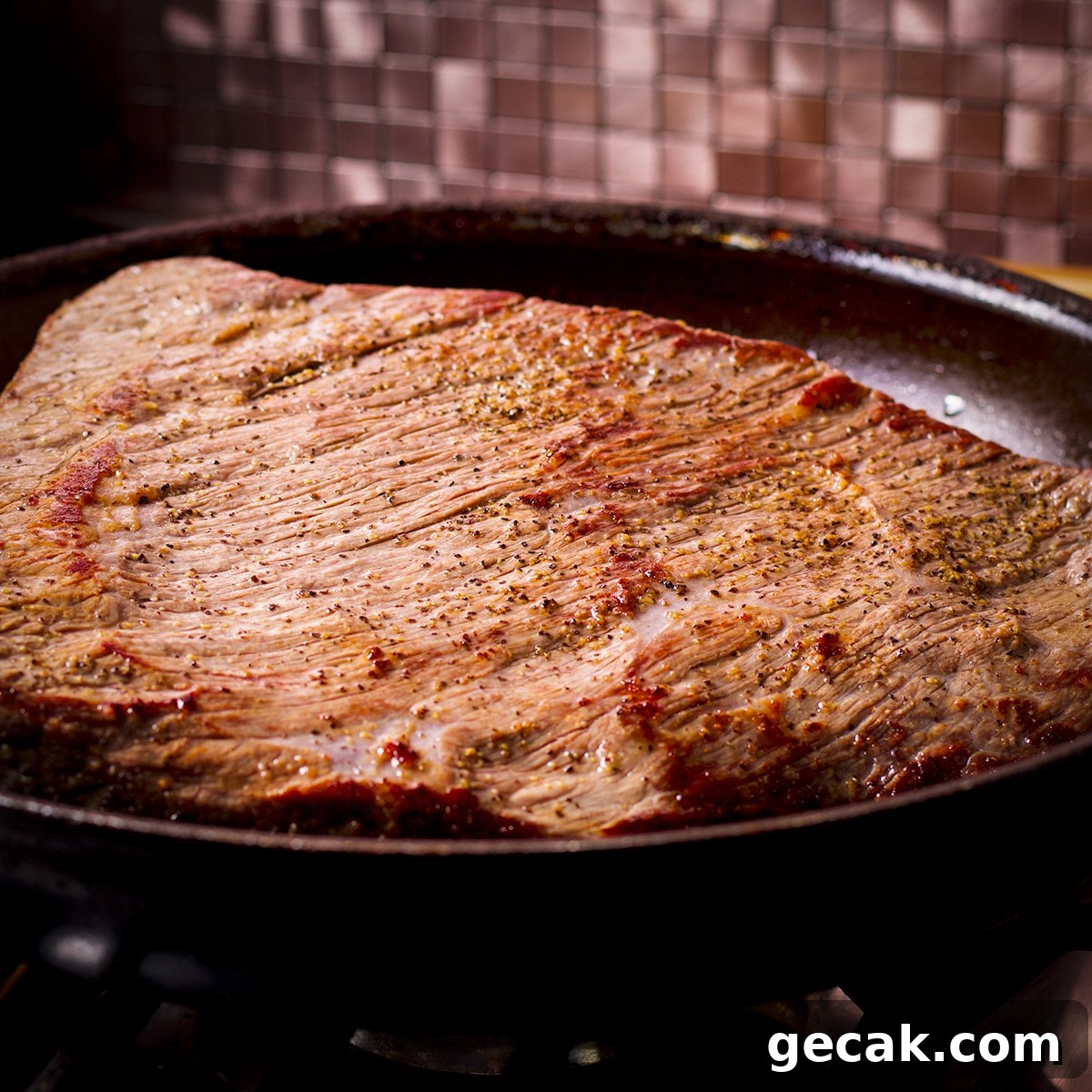 A beef brisket browning in hot oil in a skillet.