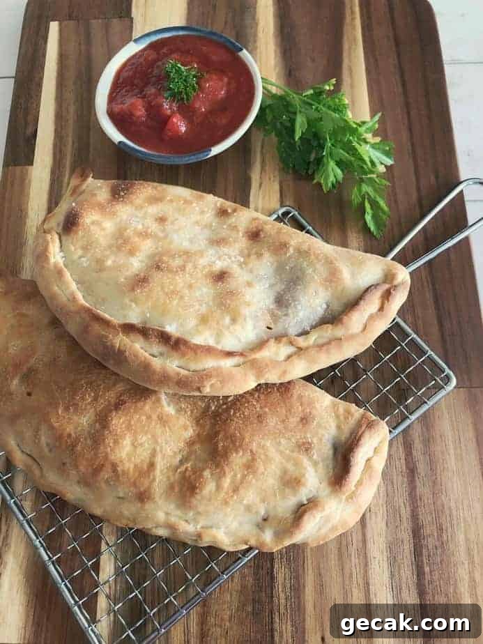 2 homemade calzone on cutting board with bowl of marinara sauce