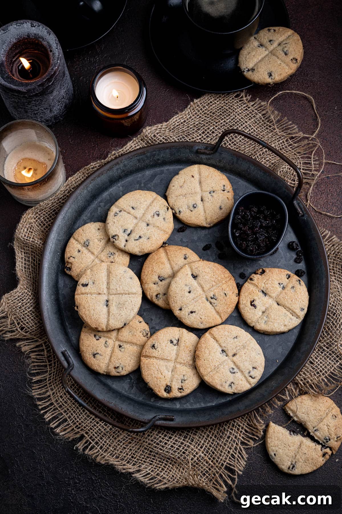 Vegan soul cakes on a metal tray on a dark surface with candles and cups of coffee.