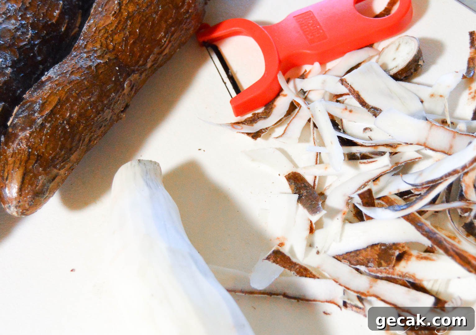 Whole yuca with a peeler and the skins peeled on a cutting board