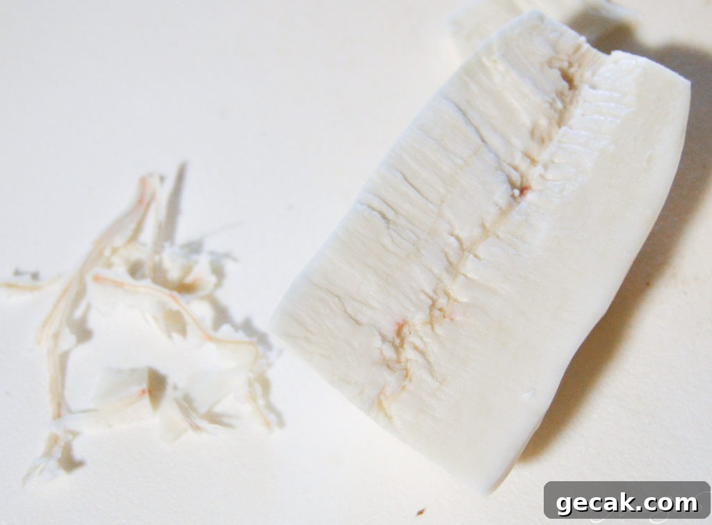 A halved yuca with some of the fibrous parts pulled out on a white cutting board