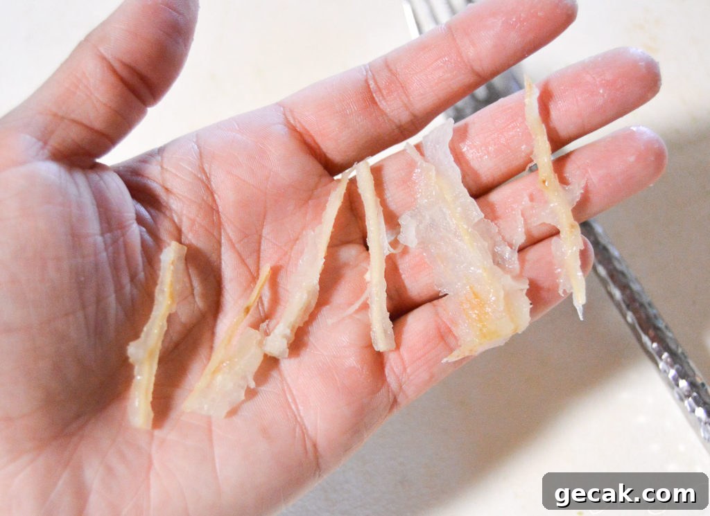 A hand holds the fibrous yuca parts above a cutting board after they've been removed from the vegetable