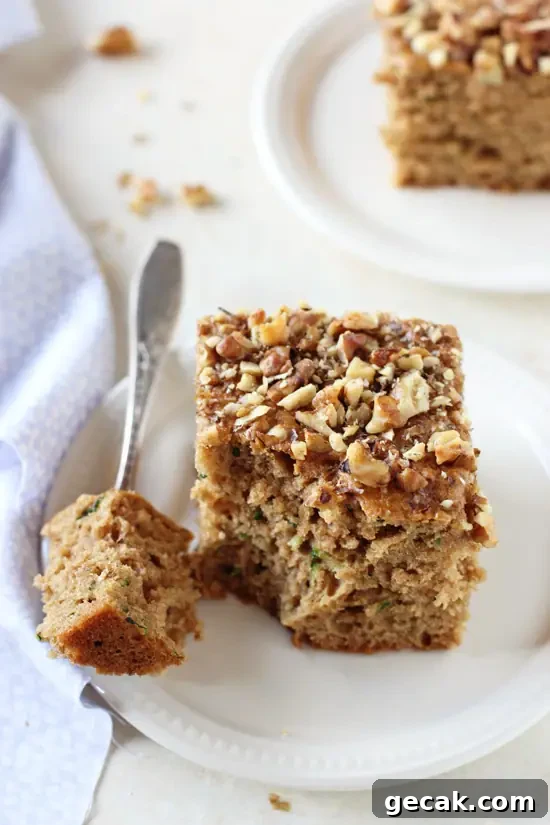 Two slices of Healthy Zucchini Bread on white plates with a fork and blue napkin to the side.