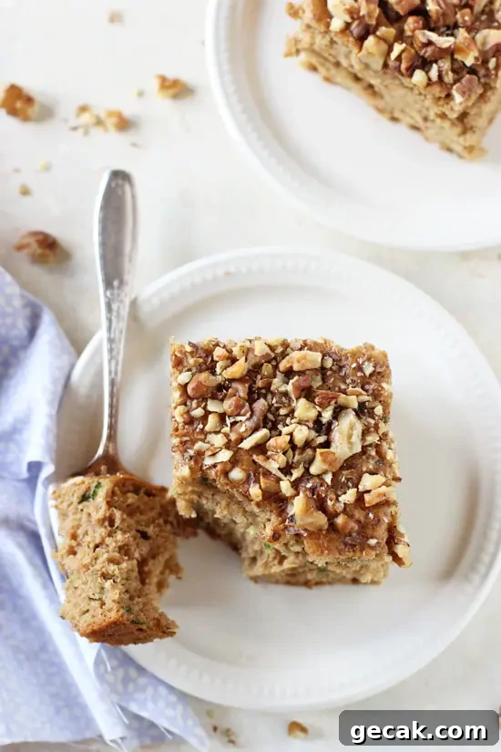 Two squares of Honey Cinnamon Zucchini Bread on white plates with a bite taken out with a fork.