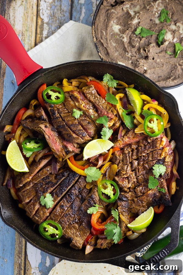 Steak fajitas in a black cast iron skillet with red and yellow bell peppers and fresh slices of jalapenos and lime.