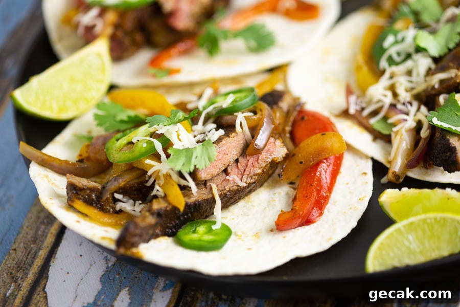 Close up of a steak fajita on a flour tortilla sitting on a black plate with lime wedges