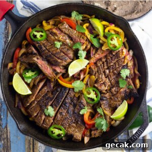Overhead view of fajita seasoned skirt steak on a bed of sauteed bell peppers and onions topped with fresh jalapeno slices and lime wedges