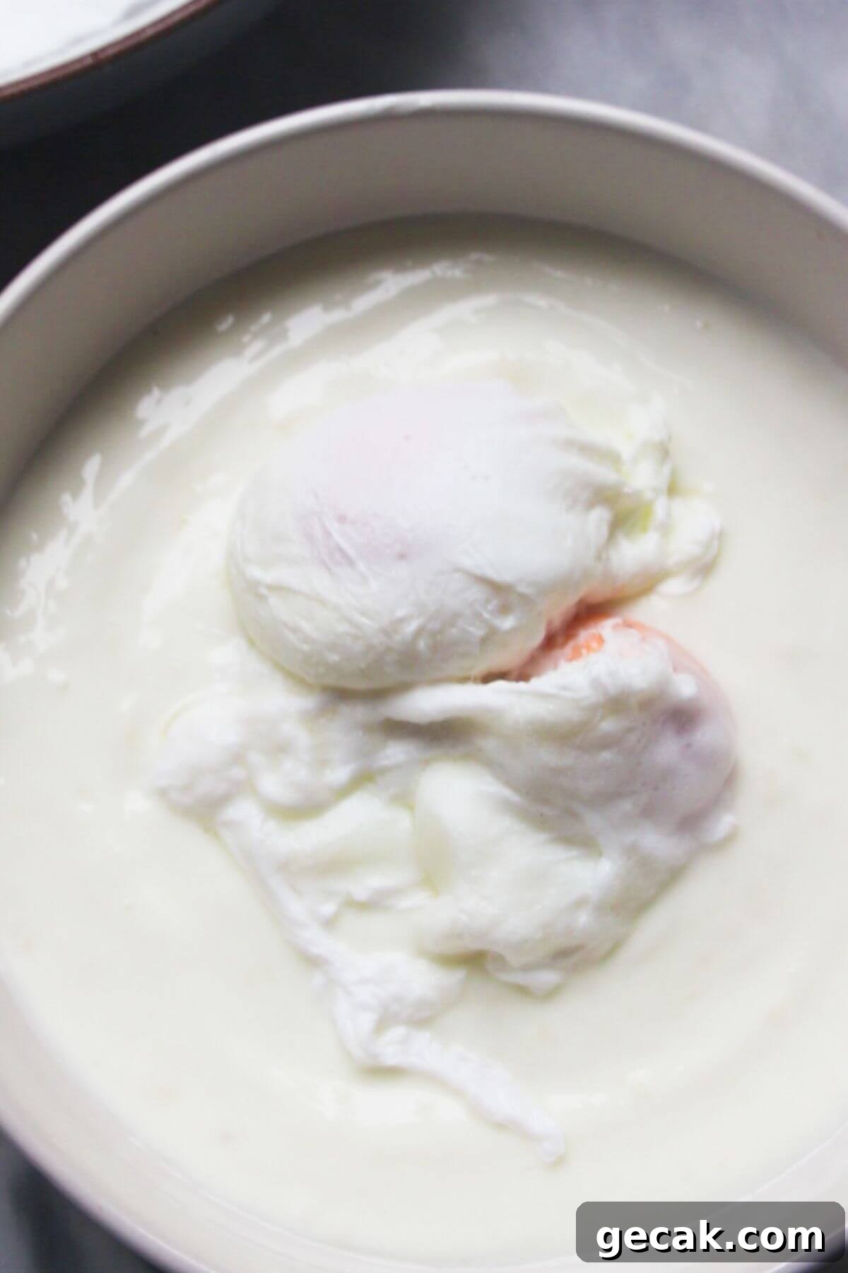 Turkish-Style Poached Eggs with Tomato and Yogurt Sauce 11 2 poached eggs sitting on top of garlicky yogurt in a small white bowl.