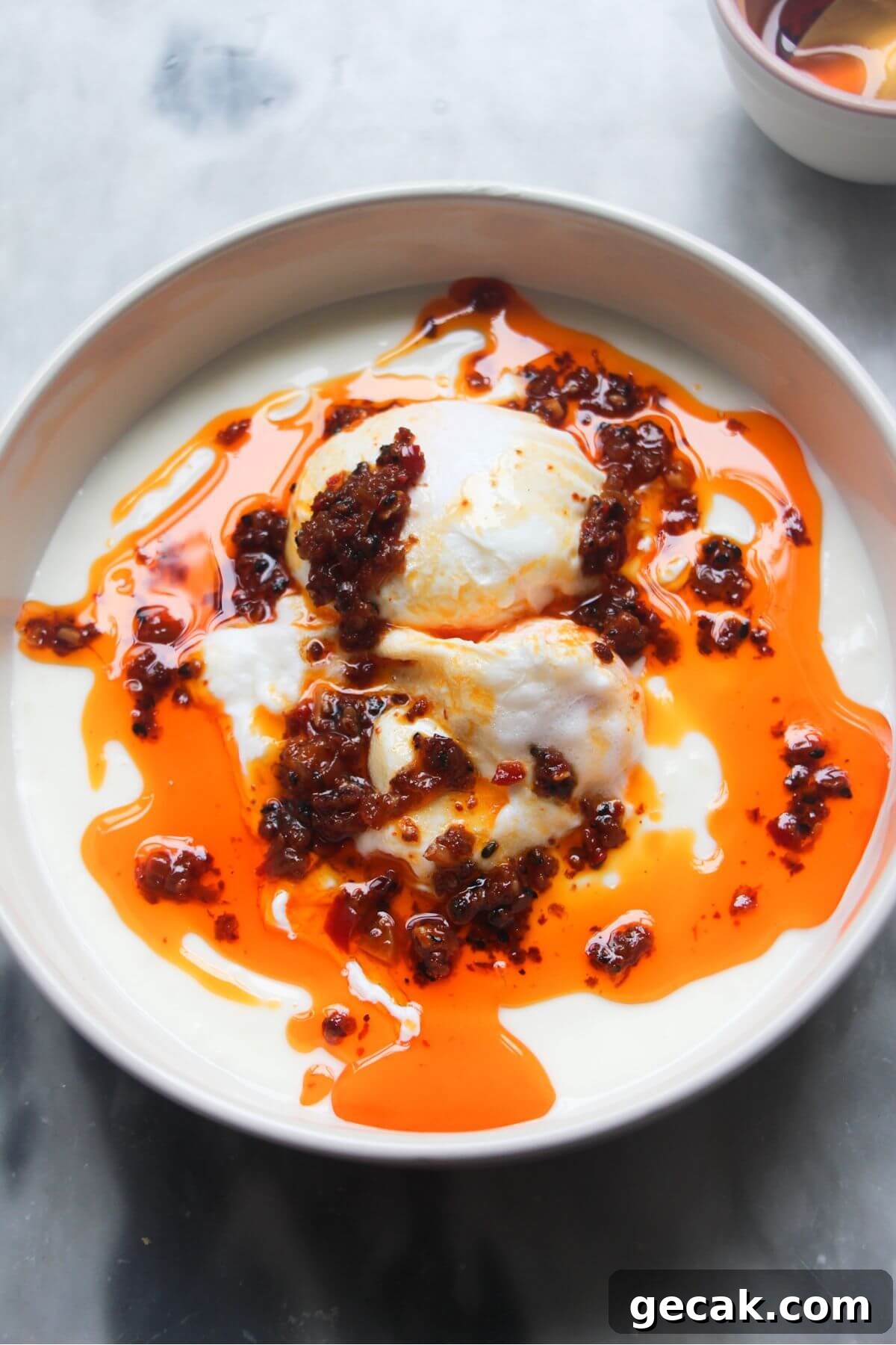 Turkish-Style Poached Eggs with Tomato and Yogurt Sauce 12 Chilli oil drizzled on top of 2 poached eggs sitting in a small bowl of yogurt.