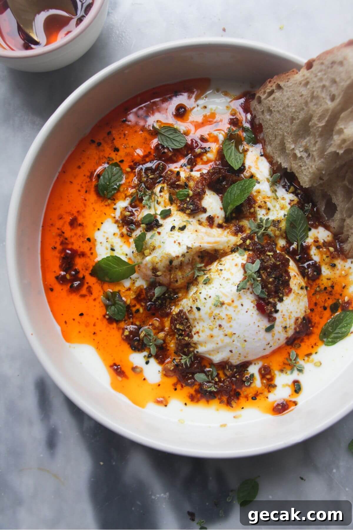 Turkish-Style Poached Eggs with Tomato and Yogurt Sauce 13 Poached eggs with chilli oil and garlick yogurt in a small white bowl with toast on the side.
