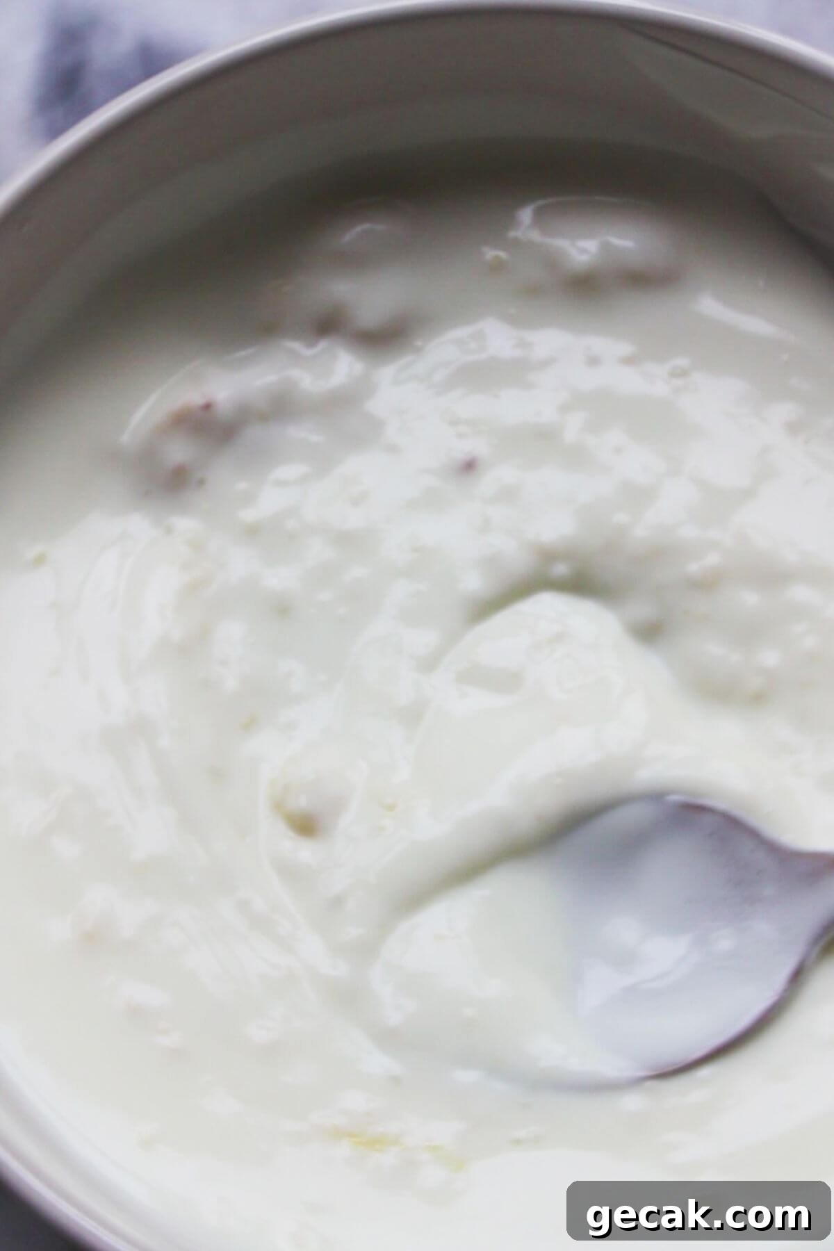 Turkish-Style Poached Eggs with Tomato and Yogurt Sauce 5 Small spoon mixing crushed garlic through yogurt in a small white bowl.