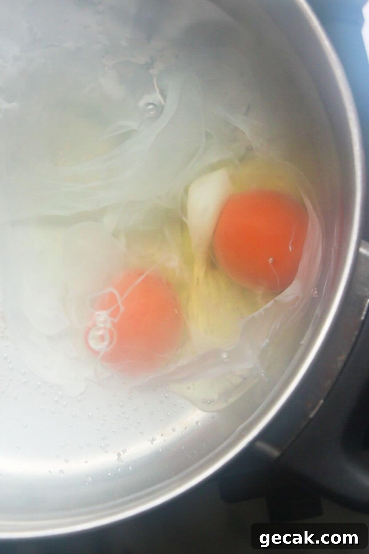 Turkish-Style Poached Eggs with Tomato and Yogurt Sauce 7 Close up of 2 eggs in water in a silver pan, starting to be poached.