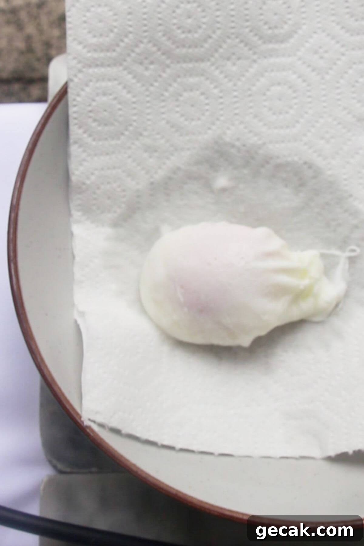 Turkish-Style Poached Eggs with Tomato and Yogurt Sauce 9 One poached egg draining on a paper towel on a plate.