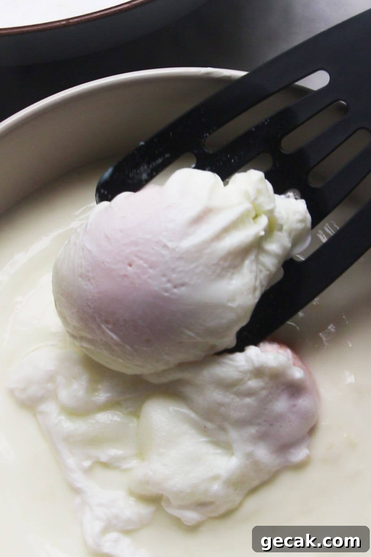 Turkish-Style Poached Eggs with Tomato and Yogurt Sauce 10 Black spatula transferring a poached egg into a bowl with garlicky yogurt.