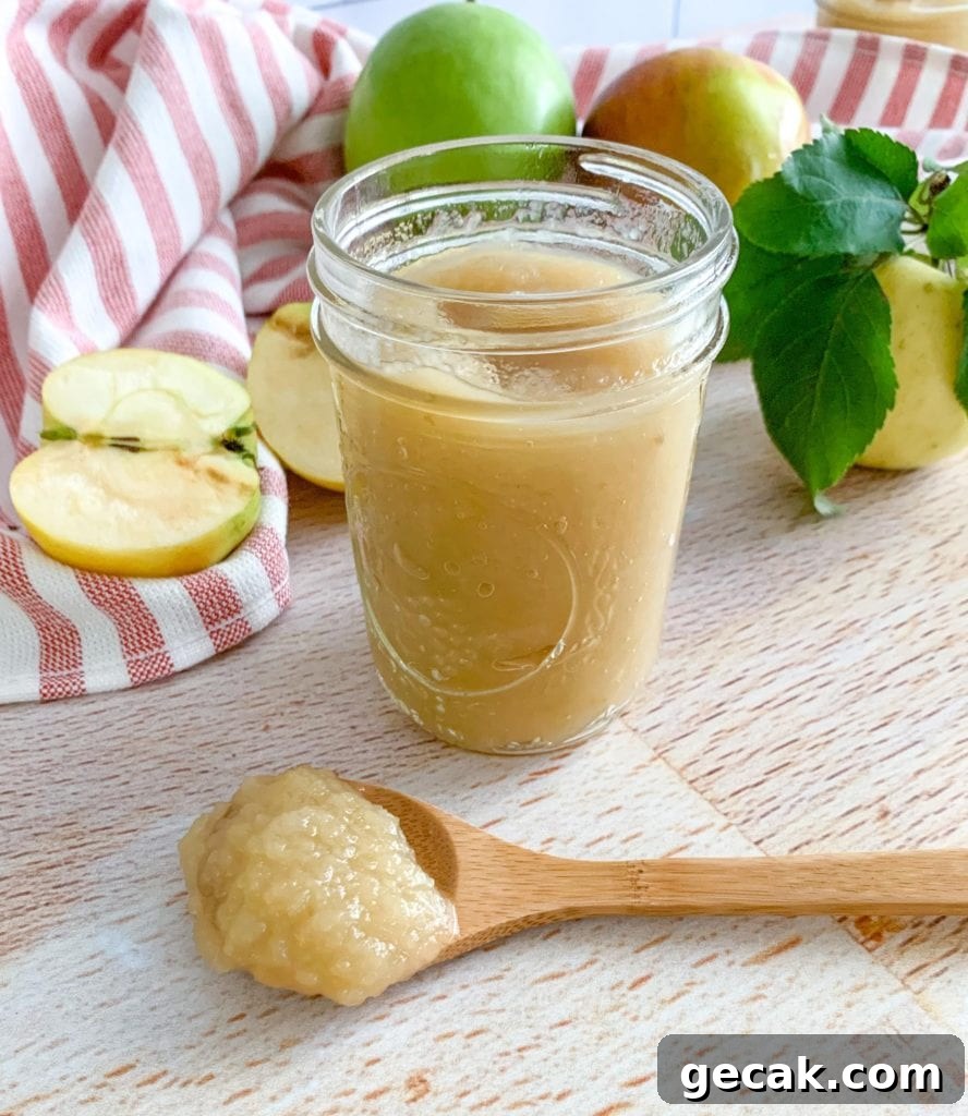 A jar of applesauce. A wooden spoon and apples in the background.