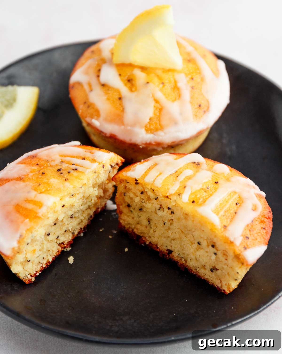 A lemon poopy seed muffin cut in half with a whole muffin behind it.