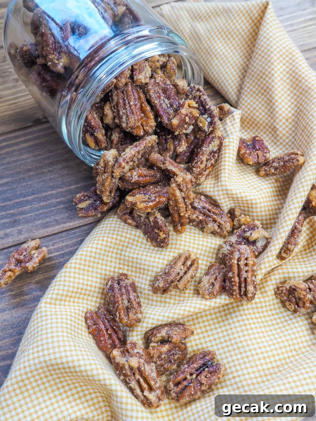 Bourbon Candied Pecans with Sweet & Spicy Glaze 11 a jar of spilled candied pecans and a yellow and white plaid napkin.