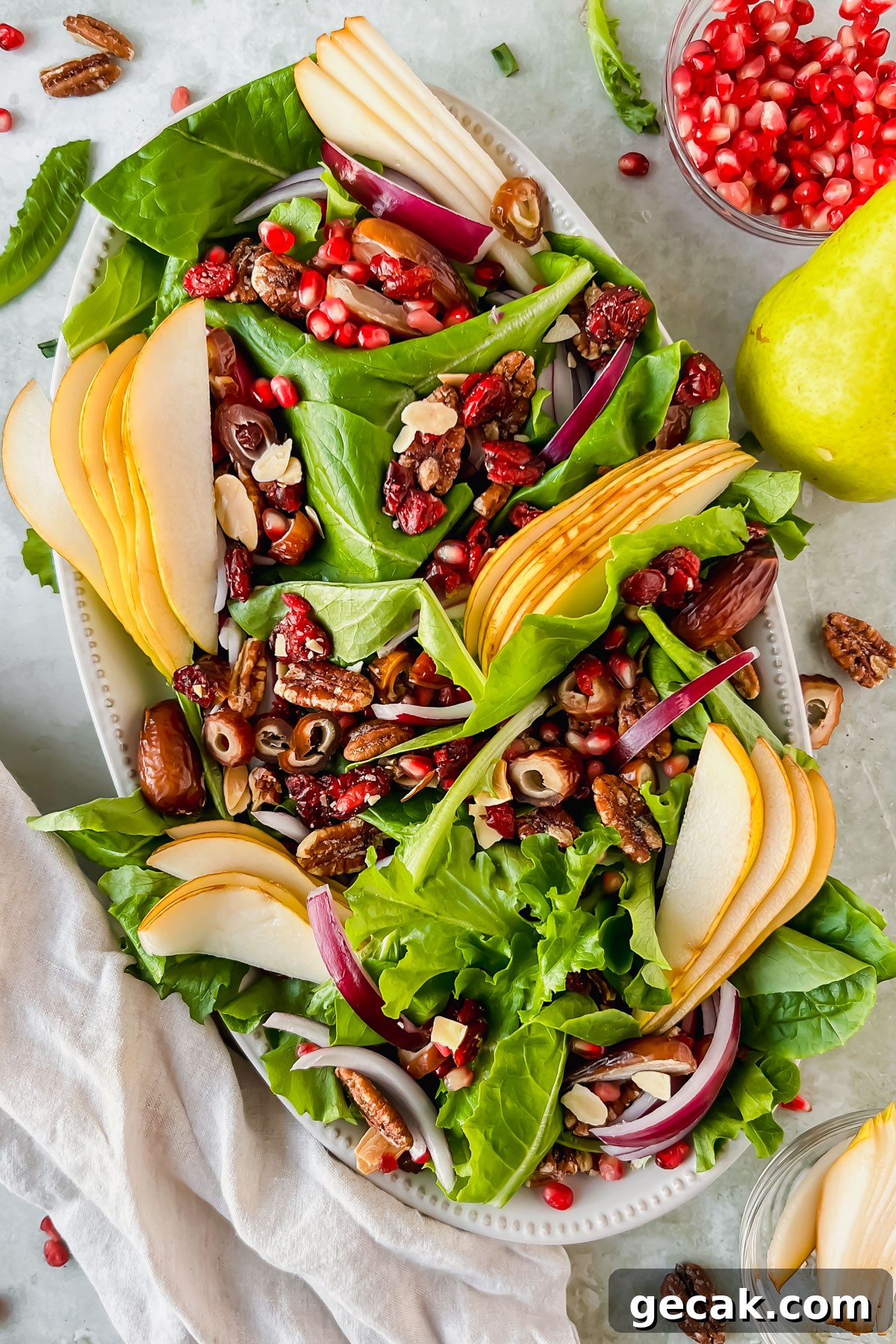 pear and pecan salad on white serving plate beside bowl of pomegranate seeds.