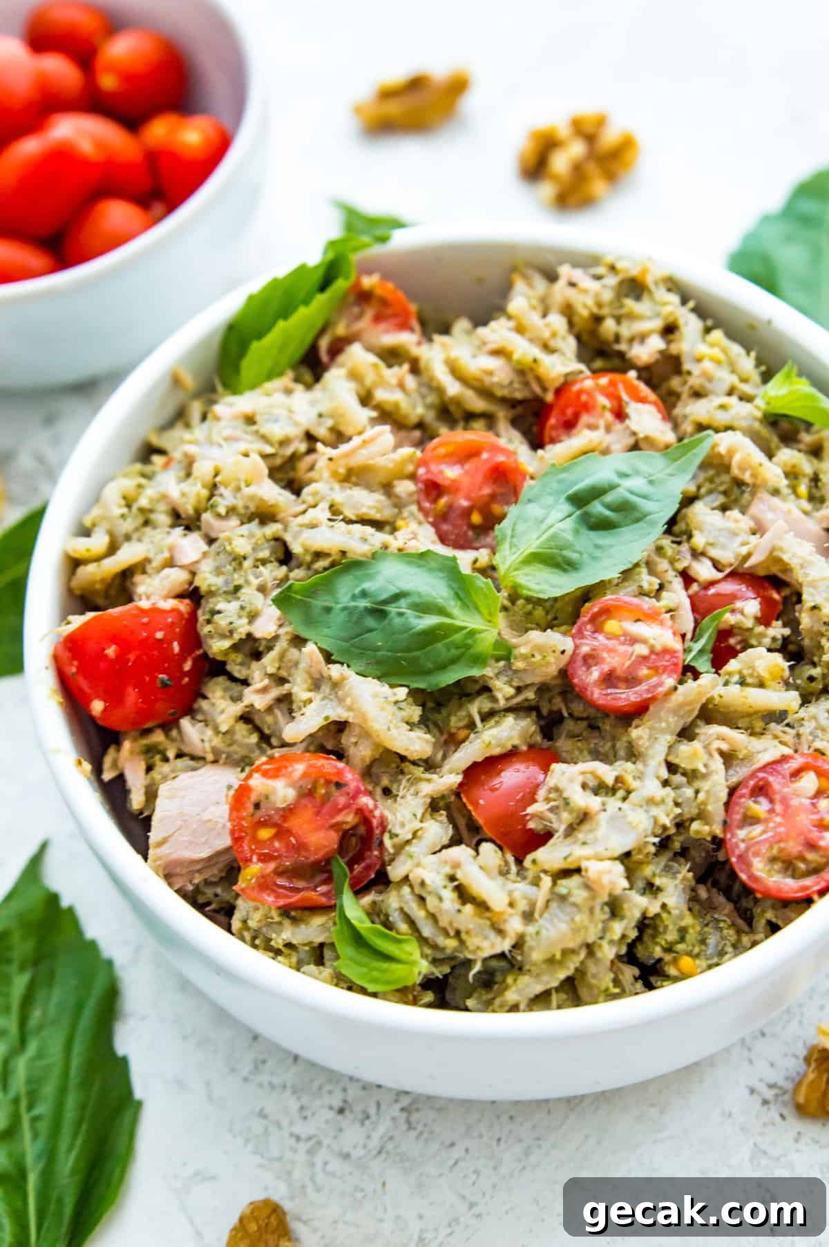 A bowl of tuna pasta pesto topped with fresh basil and chopped tomatoes.