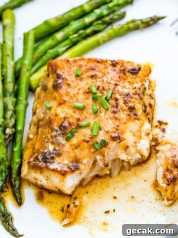 A piece of blackened cod on a plate with cooked asparagus.