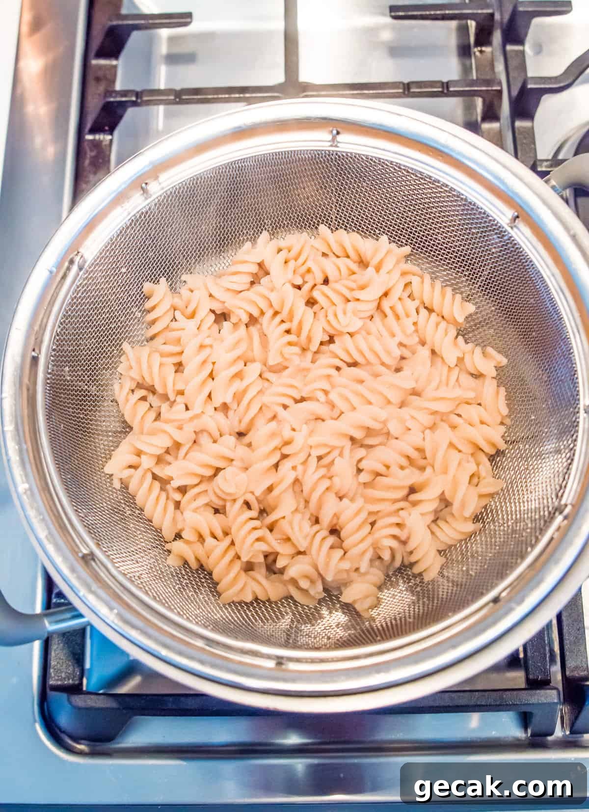 A metal colander with cooked spiral noodles in it.