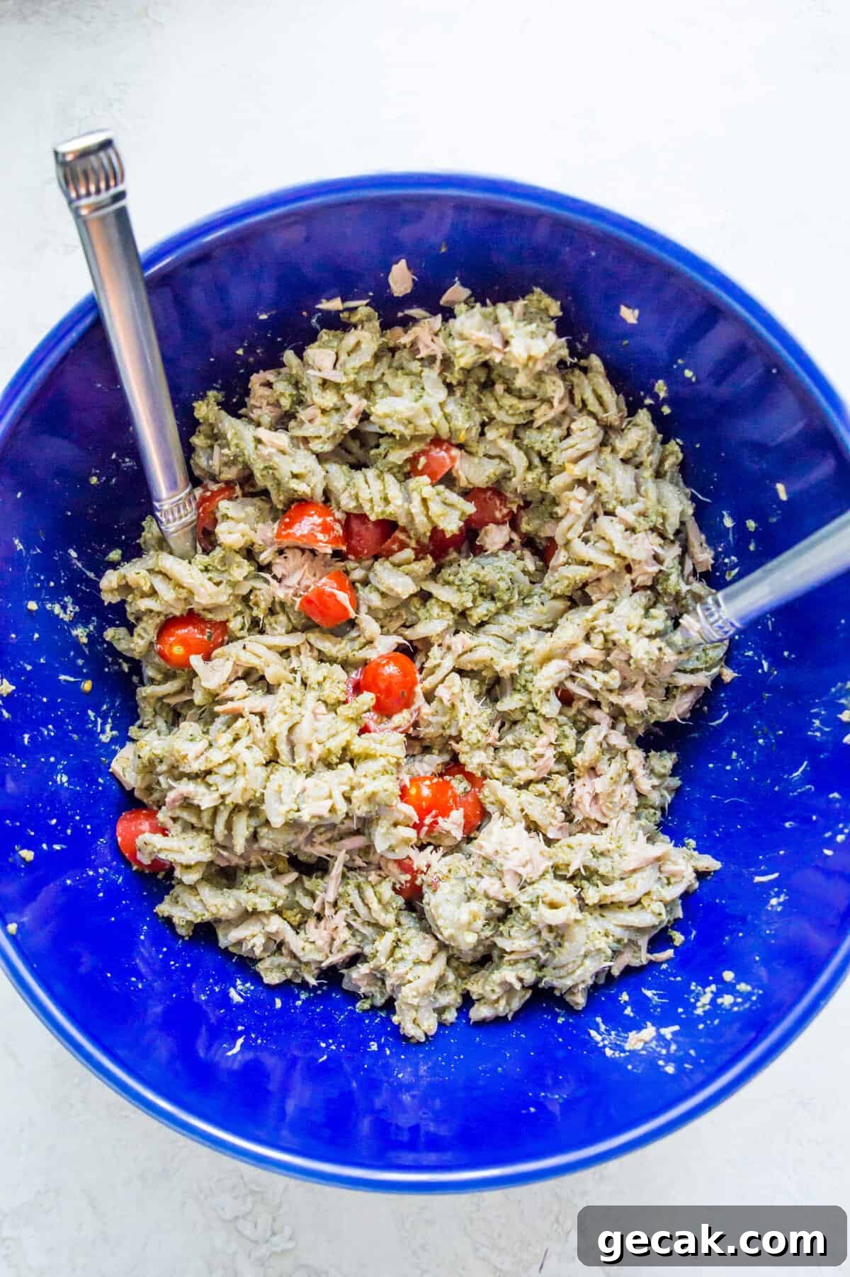 A bowl filled with cooked noodles covered in pesto sauce with chopped tomatoes on it.