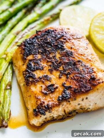 A piece of blackened mahi mahi on a plate with cooked asparagus and lime wedges beside it.