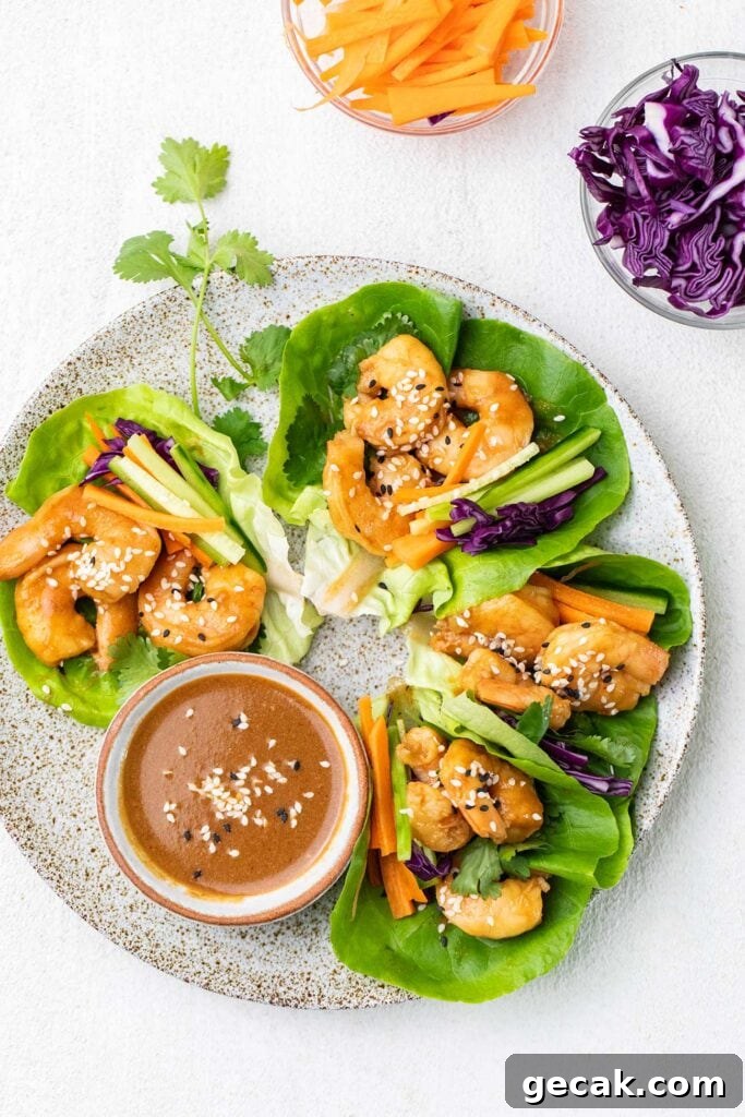 Spicy Thai Shrimp Lettuce Wraps — Low-Carb Dinner Idea 2 A plate of shrimp lettuce wraps shown with a spicy sauce and shredded vegetables.