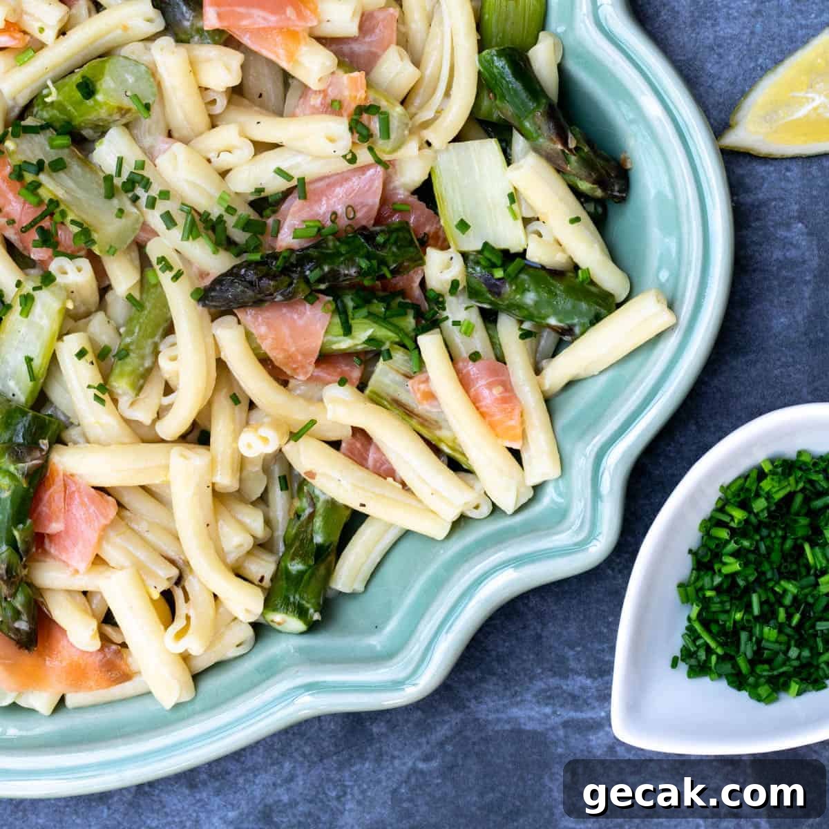 close up of smoked salmon and asparagus pasta on platter with lemon wedge and small bowl of chives