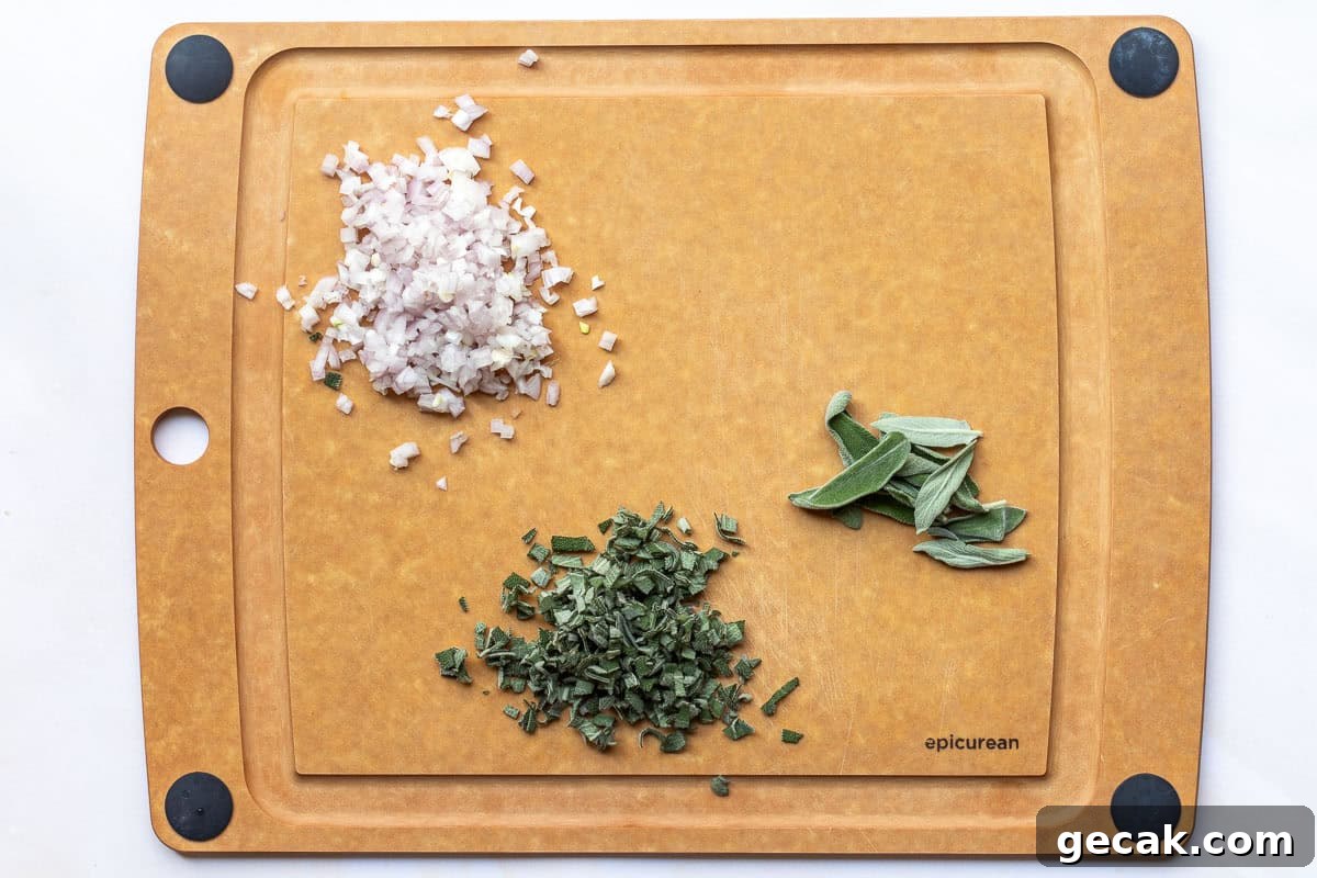 A cutting board with chopped shallots, chopped sage, and whole sage leaves arranged separately on its surface.