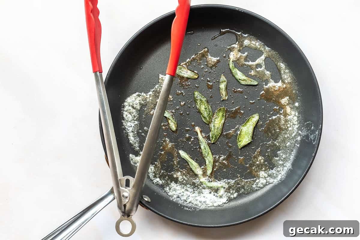 Nonstick frying pan with melted butter, browned bits, and a few fried sage leaves, with red-handled tongs resting on the edge.