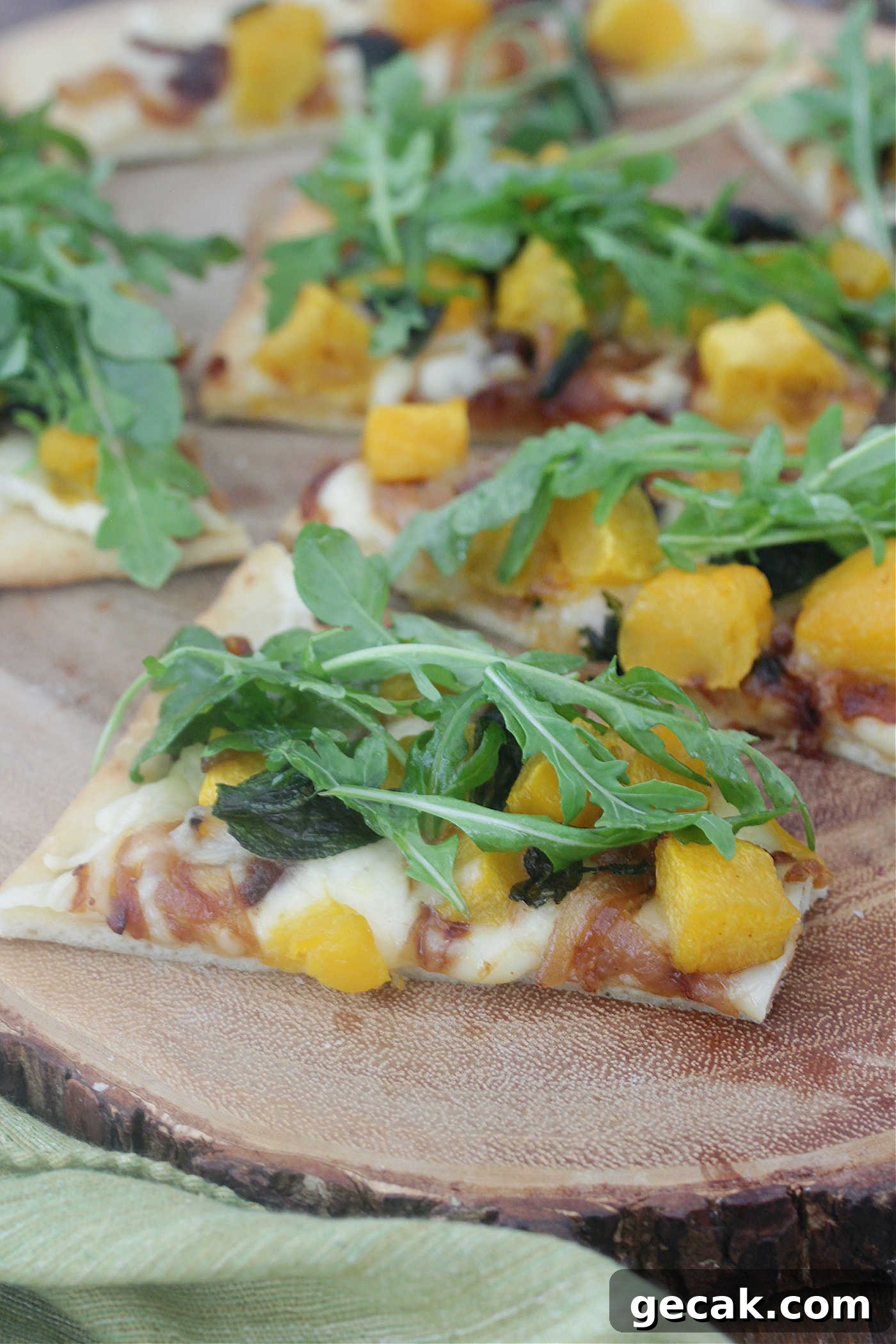 Slices of butternut squash and caramelized onions on a wooden board topped with arugula.