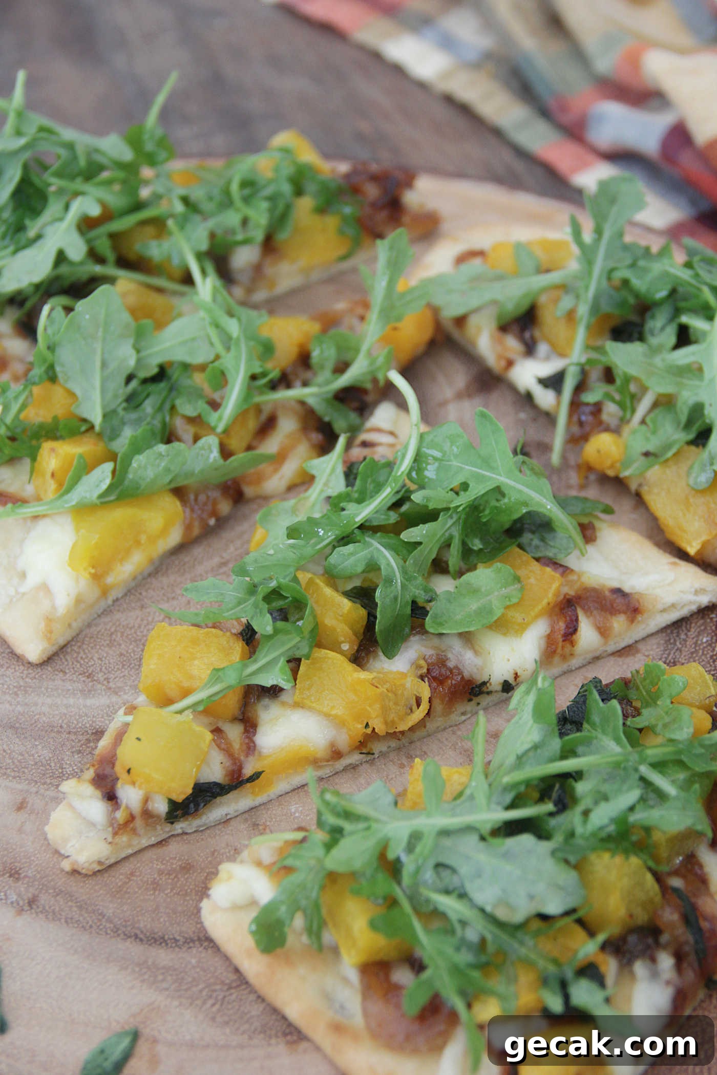 slices of flatbread pizza topped with butternut squash, caramelized onion, and arugula on a wooden board