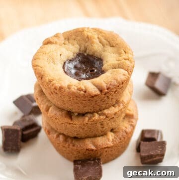 stack of cookie cups showing the cookie tops with the ganache on a white plate with pieces of chocolate