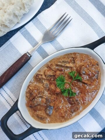 A dish of chicken livers in creamy red pepper sauce, on a blue and white striped placemat.