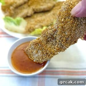 Crispy Sesame Chicken Strips Without Breadcrumbs — Low-Carb Crunch 15 A sesame-coated chicken goujon being dipped into a bowl of dipping sauce.