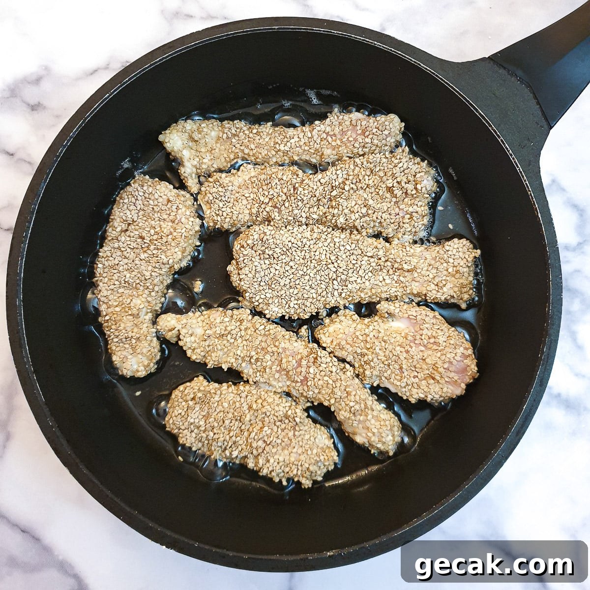 Crispy Sesame Chicken Strips Without Breadcrumbs — Low-Carb Crunch 9 Sesame chicen strips being fried in a frying pan.