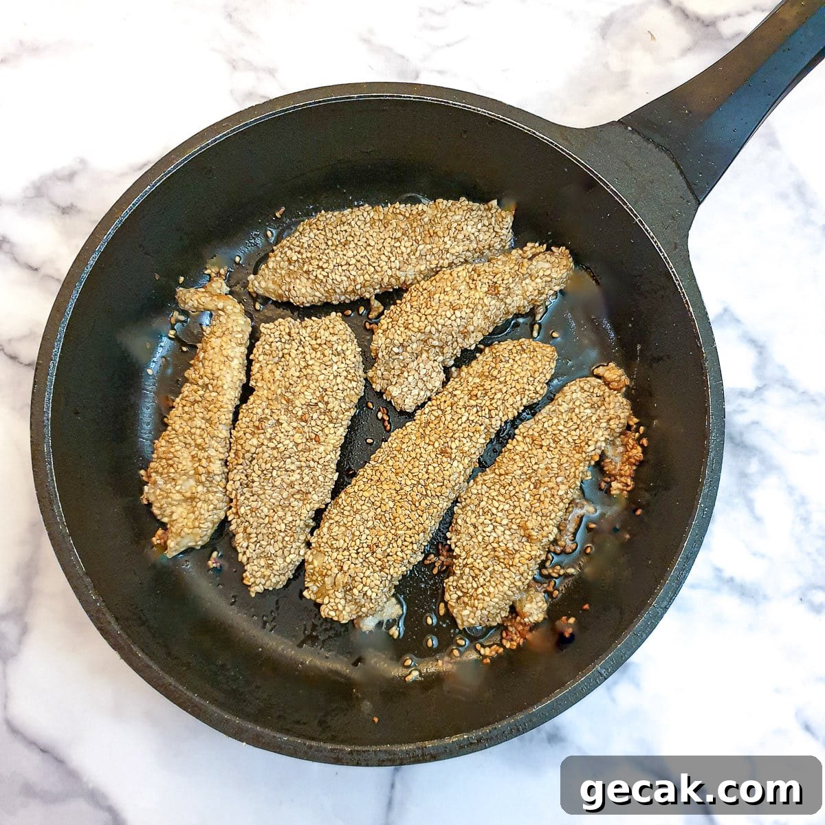 Crispy Sesame Chicken Strips Without Breadcrumbs — Low-Carb Crunch 10 Browned sesame chicken strips in a fryng pan.