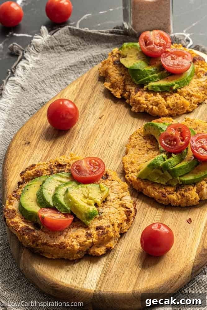 Savory Cauliflower Pancakes with Herbs and Parmesan 2 savory pancakes on a wood cutting board topped with avocado and tomatoes