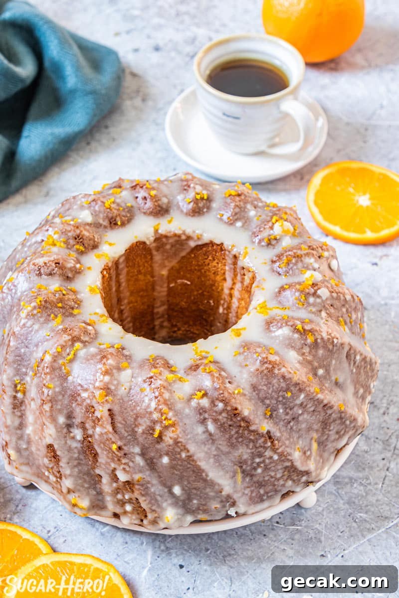 Orange bundt cake with orange glaze, with coffee cup and teal napkin in background.