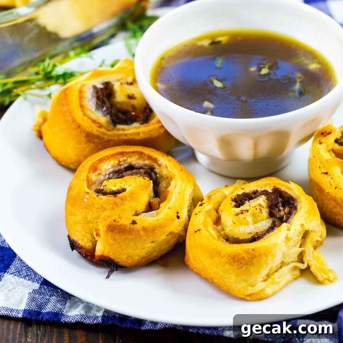 French Dip Pinwheels Recipe — Savory Roast Beef Appetizer 2 French Dip Pinwheels on a plate with a bowl of Au Jus.