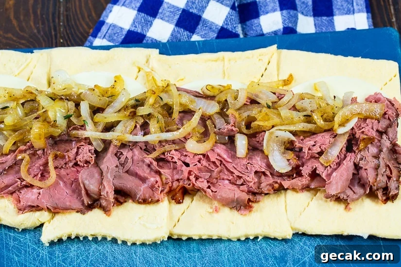 French Dip Pinwheels Recipe — Savory Roast Beef Appetizer 4 Roast beef and onions spread out on crescent roll dough.