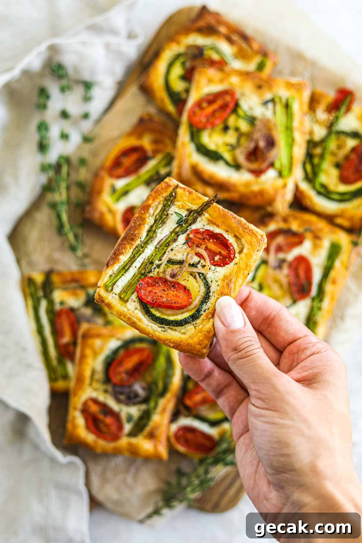 Savory Puff Pastry Vegetable Tarts for Entertaining 6 Photo of hand holding a goat cheese puff pastry vegetable tart.