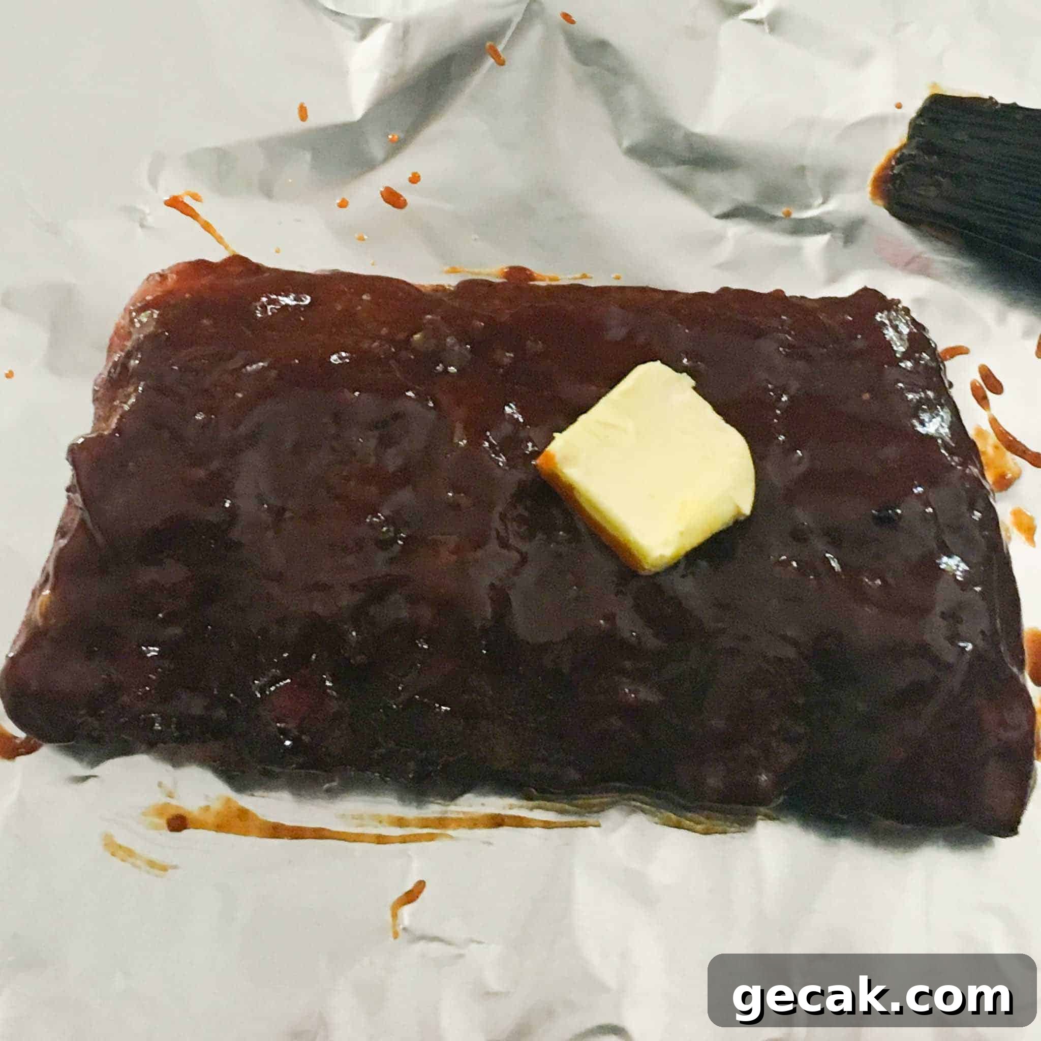 Rack of ribs slathered in sauce with pad of butter on top overhead shot